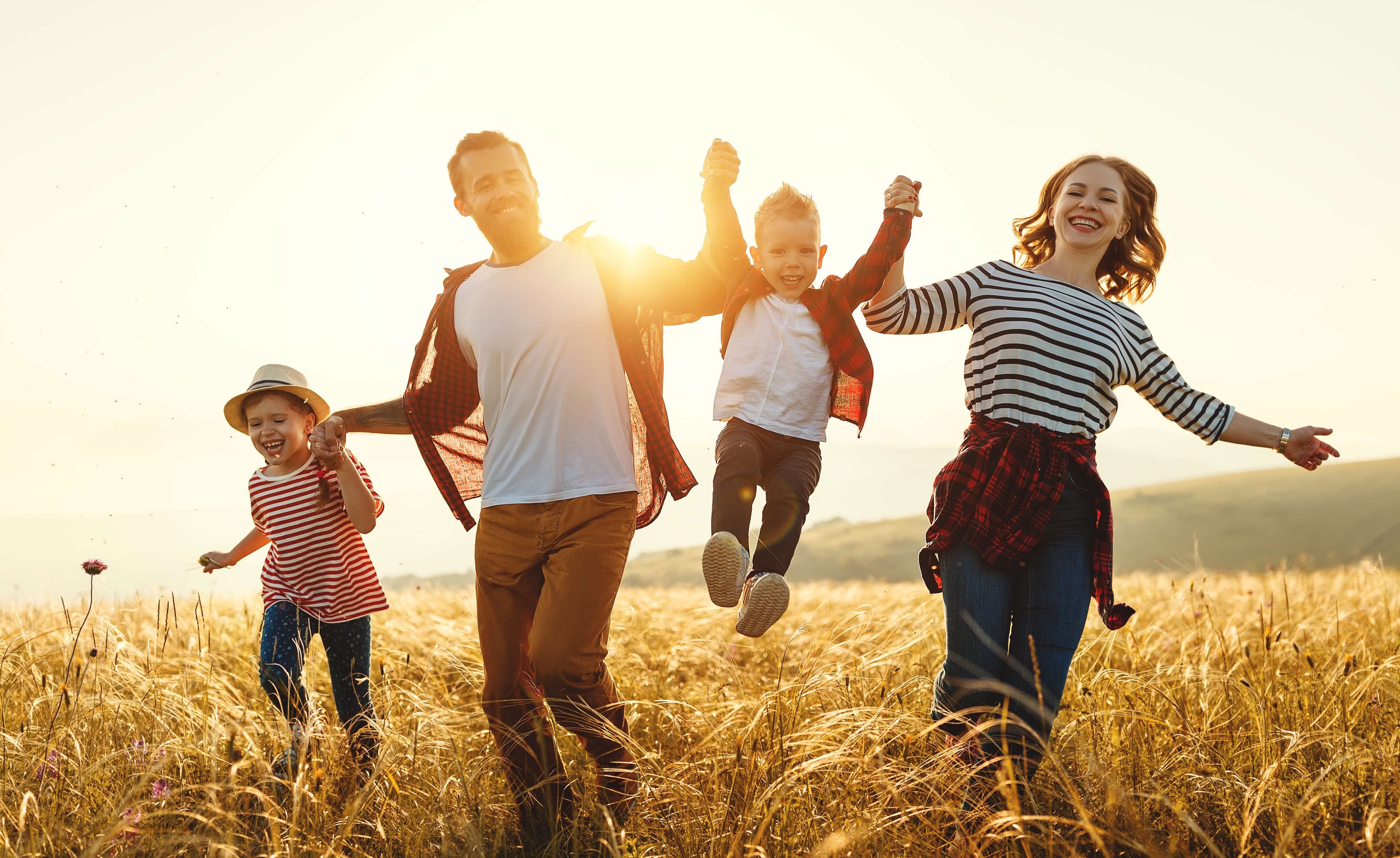 Caucasian parents and kids smiling while running through a field