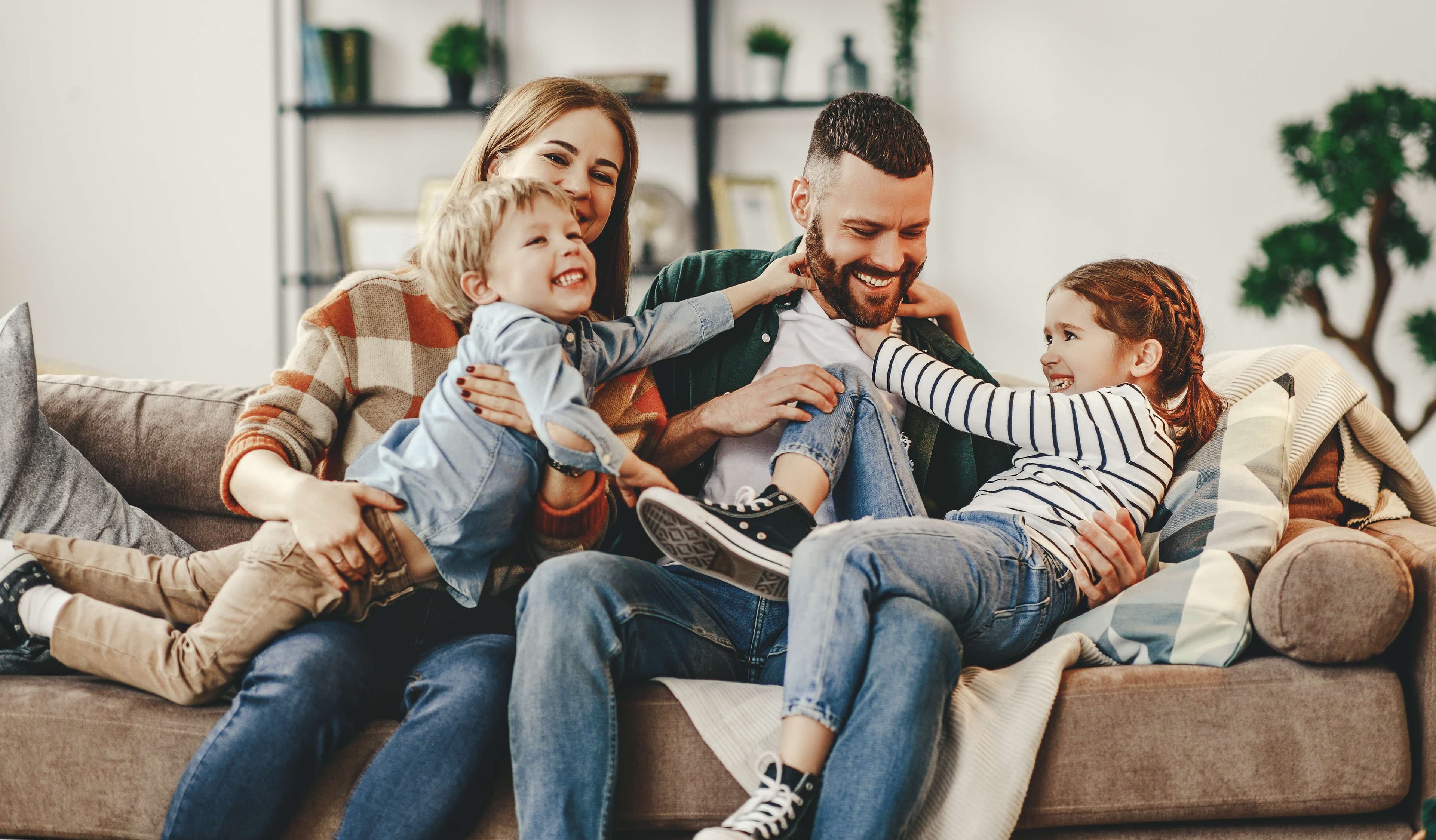 Caucasian parents and two kids smiling and playing on a couch