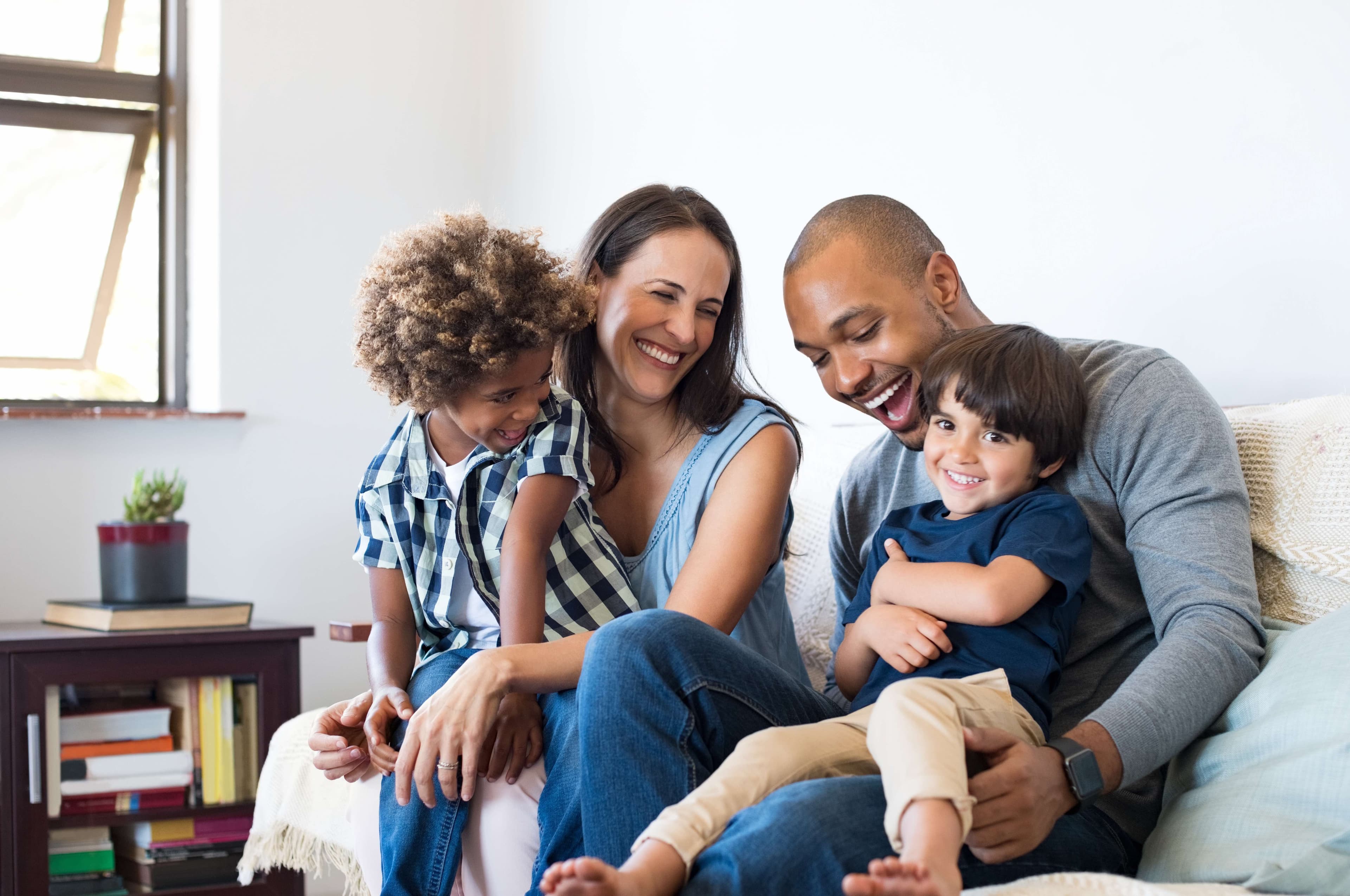 Caucasian mom and black dad with two son smiling on a couch